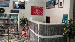 A hotel reception area with a marble reception desk, a chandelier, a red banner, and framed pictures on the wall.