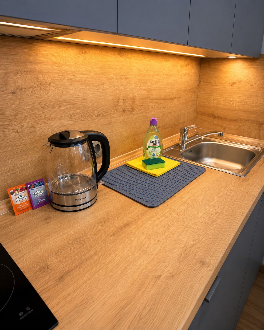 Ett kök med en kaffebryggare, en flaska diskmedel och en svamp på en köksmatta.