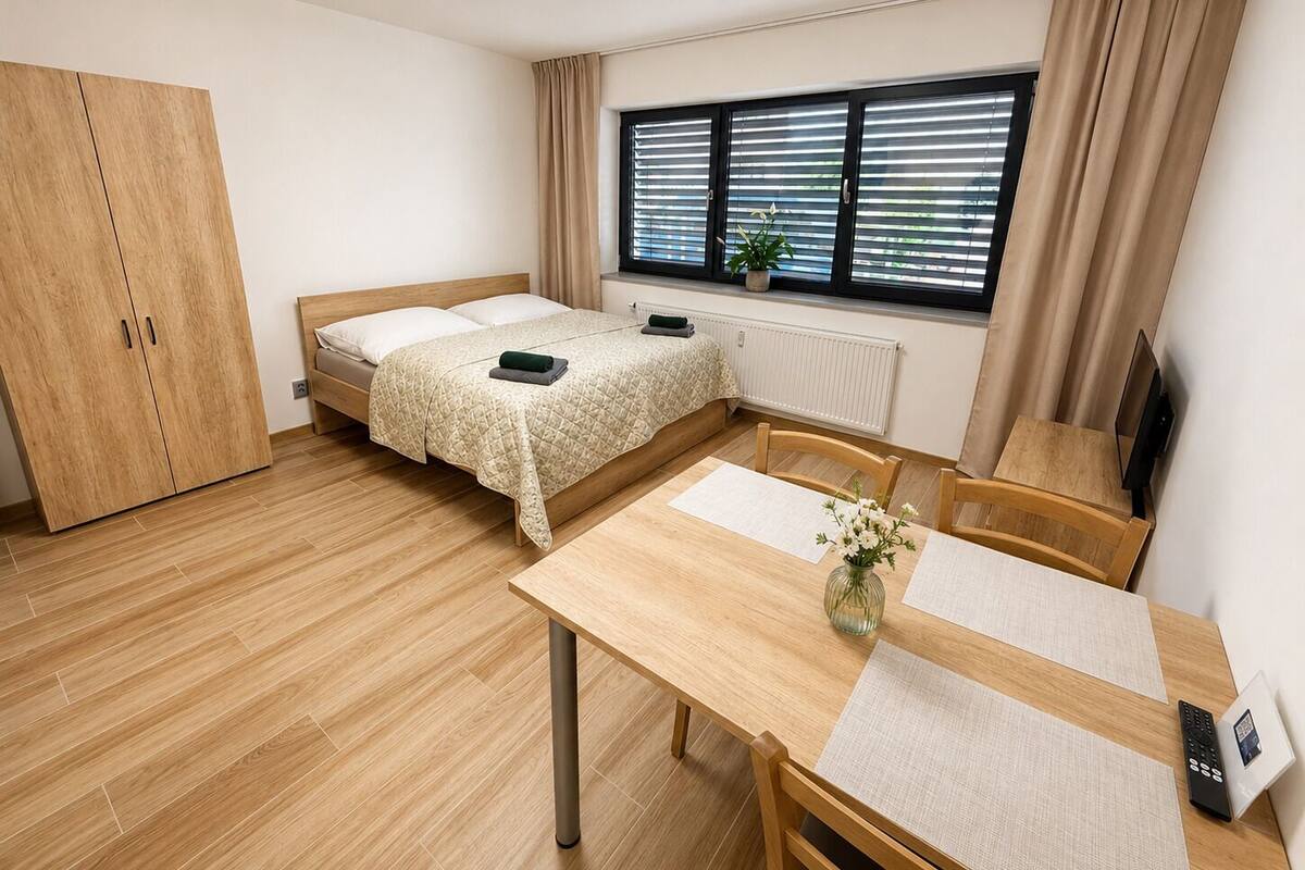 A room with a bed, a desk, a chair, a wardrobe, a window with blinds, and a radiator.