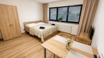 A room with a bed, a desk, a chair, a wardrobe, a window with blinds, and a radiator.