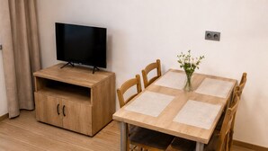 A wooden dining table with four chairs, a television on a wooden stand, a cabinet with two doors, and a small vase with flowers on the table. - Microbyty & Apartments  (Ústecký kraj)