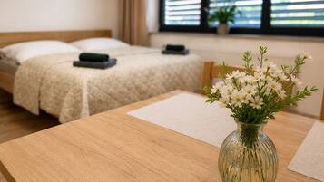 Een hotelkamer met twee bedden, een houten tafel met een bloemenvaas en een raam met jaloezieën.