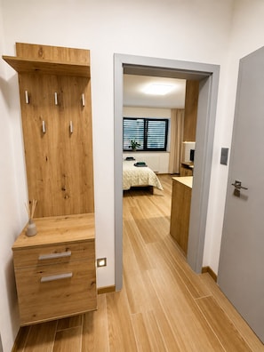 Ein Schlafzimmer mit einem Holzschrank, einem Bett mit gemustertem Überwurf, einem Fenster mit Jalousien und einem Nachttisch mit Lampe.
