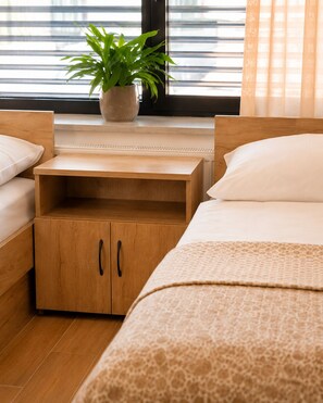 A bedroom with two beds, a nightstand, a wooden cabinet, and a potted plant.