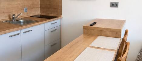 A modern kitchen with a wooden countertop, a sink, and cabinets. There is a small table with two chairs and a painting of coffee cups on the wall.