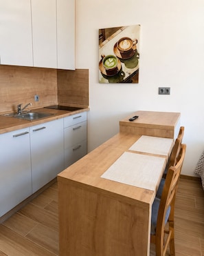 Eine moderne Küche mit Holzarbeitsplatte, Spüle und Schränken. Es steht ein kleiner Tisch mit zwei Stühlen da, an der Wand hängt ein Bild von Kaffeetassen.
