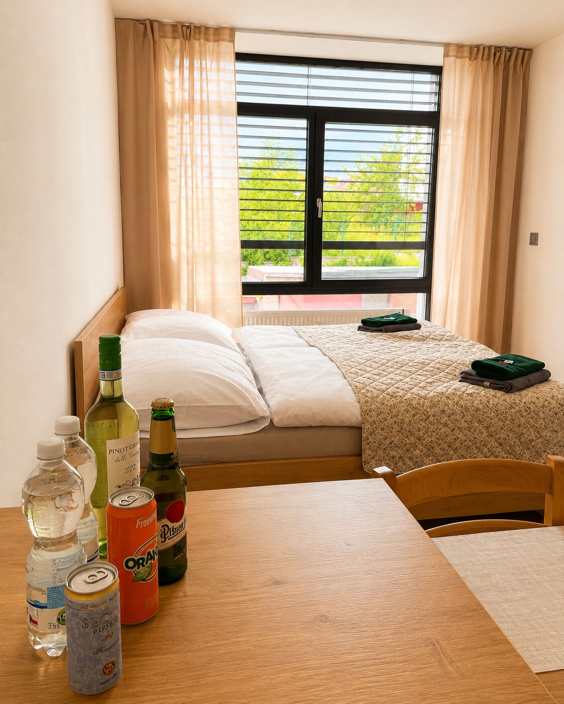 A bedroom with a bed, a table with bottles and cans, and a window with curtains.
