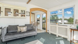 A living room with a grey sofa, a wooden archway, a white cabinet with glass doors, and a view through large windows.