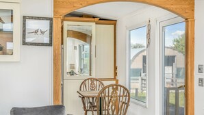 A cozy room with a wooden ceiling, a dining table with chairs, a gray sofa, and a large window with a view of the outside.