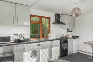 Une cuisine compacte avec des meubles blancs, un lave-linge, un four à micro-ondes, un grille-pain, un évier et une cuisinière.