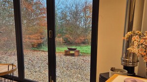 Une pièce dotée d’une grande porte-fenêtre coulissante qui donne sur un espace recouvert de gravier, agrémenté d’arbres et d’un banc en bois.