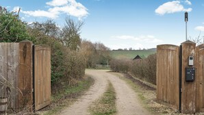 Un chemin de terre qui traverse la campagne et mène à un portail en bois, entouré de végétation, sous un ciel dégagé.