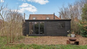 Une maison moderne dotée d’une grande porte vitrée, d’une cheminée et d’un petit jardin.