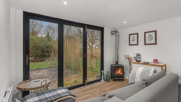 Un salon moderne comprenant un canapé, une petite table, une cheminée et une porte-fenêtre coulissante donnant sur un jardin.