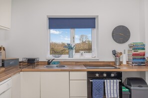 A modern kitchen with a window, sink, and a clock on the wall. - Rosie's Retreat - Charming Farmhouse Stay (Charndon)