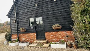 Une maison en bois avec une porte noire, des fondations en briques et une allée gravillonnée.