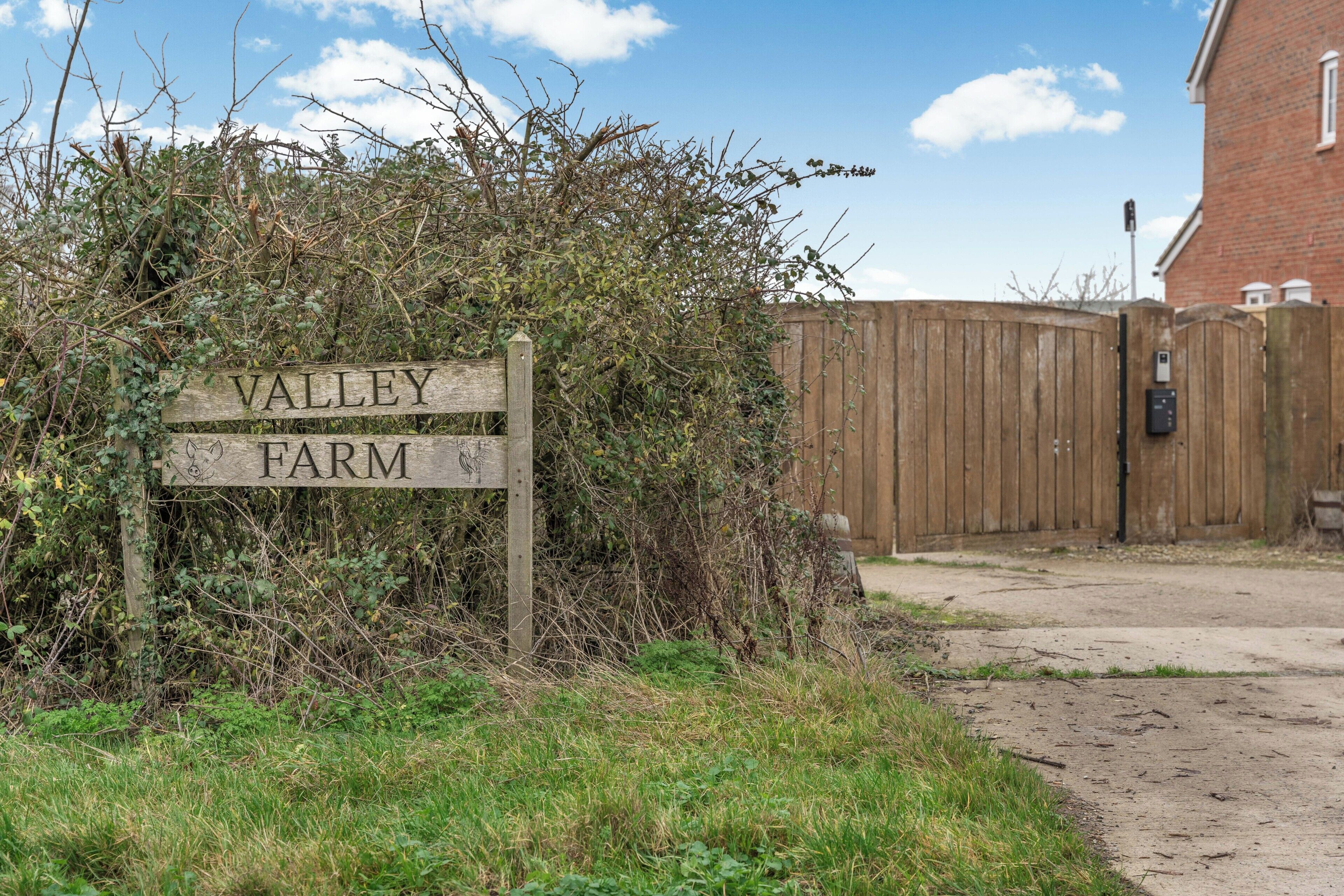 Een houten bord met de tekst 'VALLEY FARM', omringd door overwoekende begroeiing.