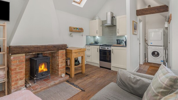 A loft-style room with a fireplace, kitchen, and laundry area. - The Nook - Cosy Rural Cottage with Stunning Views (Charndon)