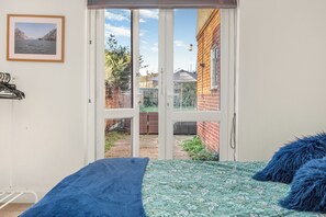 Et soveværelse med en seng, et blåt tæppe, et billede i ramme på væggen og en skydedør, der fører til en have.