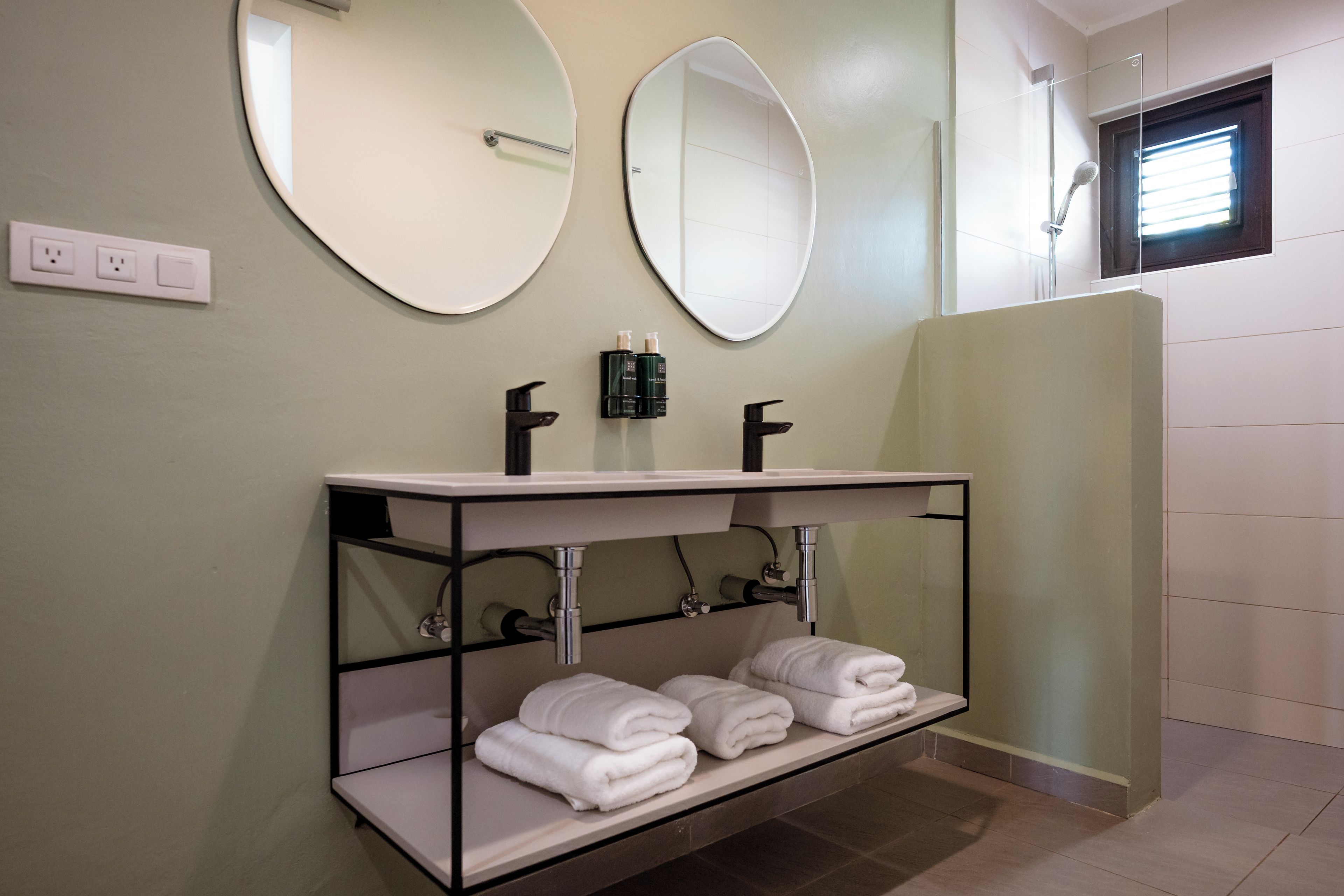 A bathroom with two round mirrors, a white sink with a black faucet, and a shelf with folded towels.