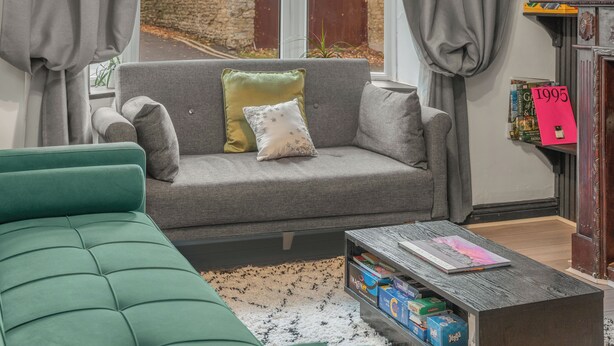 Una sala de estar con un sofá gris, un sillón verde y una mesa de centro con libros.