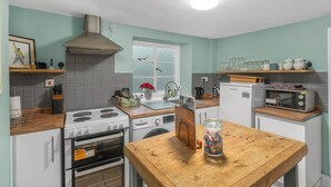 Una cocina con estufa, horno, microondas y una mesa de madera con un tarro de aperitivos.