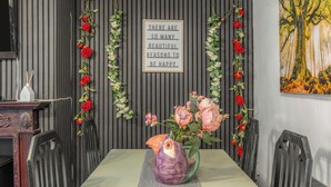 Un área de comedor con una mesa preparada para dos, un jarrón decorativo con flores, un letrero en la pared y un cuadro.