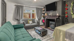 Una sala de estar con un sofá verde, una chimenea, un televisor de pantalla plana y una estantería.