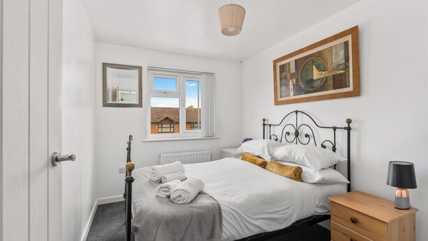 A bedroom with a bed, a wooden nightstand, a lamp, a window with a view of a house, and a painting on the wall. - Badger Haven, Apt 3 1st floor self contained apartment in Brackley (Brackley)