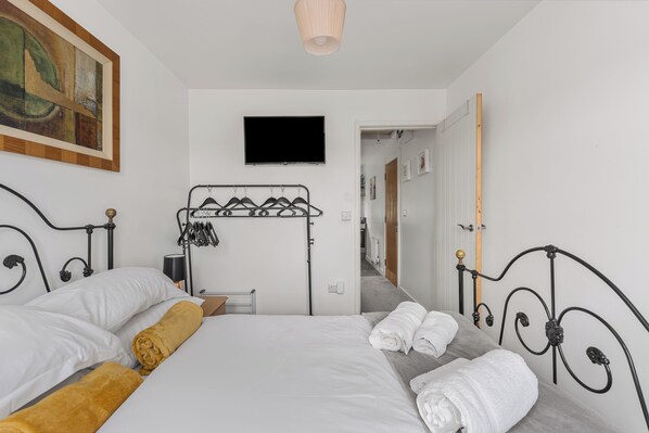 A hotel room with a bed, a TV, a coat rack, and a painting on the wall.