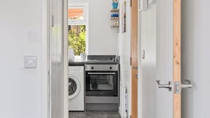 A compact kitchen with a washing machine, oven, and a window with a view of greenery. - Badger Haven, Apt 3 1st floor self contained apartment in Brackley (Brackley)