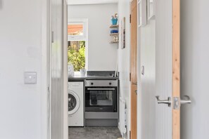 A compact kitchen with a washing machine, oven, and a window with a view of greenery. - Badger Haven, Apt 3 1st floor self contained apartment in Brackley (Brackley)