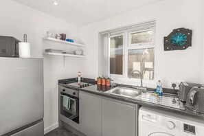 A modern kitchen with a built-in oven, a dishwasher, a sink, and a window. - Apartment 1: Badger Haven - Cozy Stay near Town Centre (Brackley)