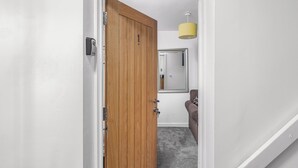 Un pasillo con una puerta de madera, un espejo y una lámpara colgante amarilla.