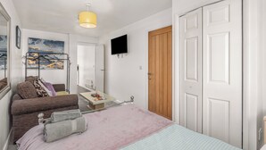 Un dormitorio con cama, televisor, puerta de madera y espejo.