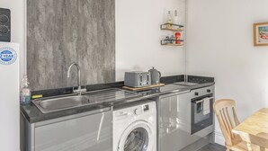 Een kleine keuken met een wasmachine, een gootsteen, een broodrooster en een houten stoel.