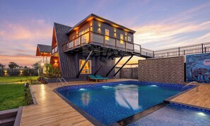 A modern house with a swimming pool, a deck, and a view of the sunset.