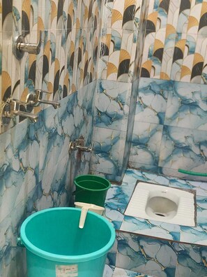 A bathroom with a toilet, a green bucket, and a green cup.