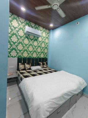 A bedroom with a bed, a ceiling fan, an air conditioning unit, and patterned wallpaper.