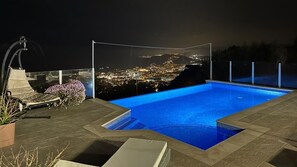 Une piscine sur le toit offrant une vue sur la ville, entourĂ©e de mobilier dâextĂ©rieur et dâune pergola.