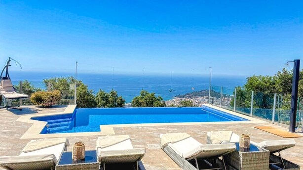 En pool med utsikt över havet, utomhusmöbler och en klar himmel.