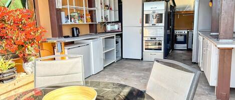 A compact kitchen with a microwave, oven, and refrigerator. There is a dining area with chairs and a table.