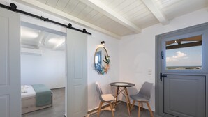 A room with a bed, a small table, two chairs, a mirror, and a view through a door. - Paros Golden Beach flats Casa Costa Azor - 33m from beach, sleeps 6 (3BDR 2BA) (Paros)