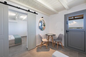 Ein Zimmer mit einem Bett, einem kleinen Tisch, zwei Stühlen, einem Spiegel und Blick durch eine Tür.