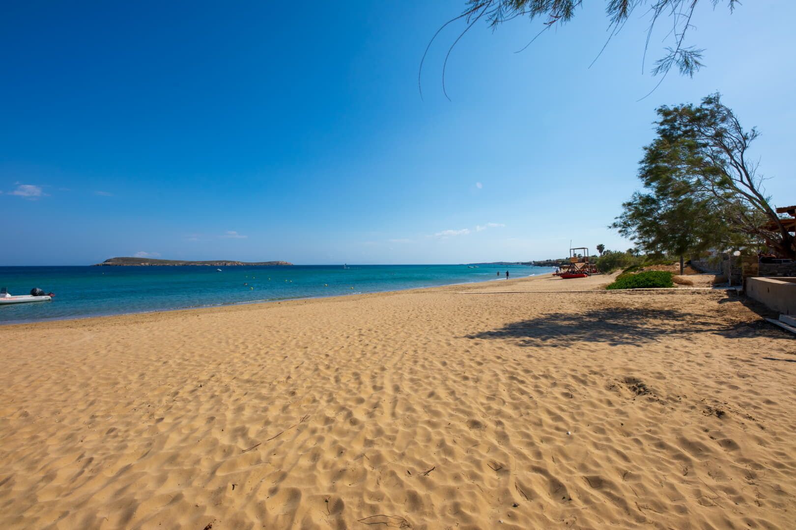 Ein Sandstrand mit blauem Himmel, einem Boot im Wasser und einem Baum auf der rechten Seite.