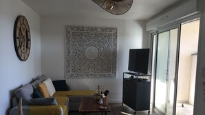 Un salon comprenant un canapé, une table basse, une horloge murale, un téléviseur posé sur un meuble et une grande fenêtre.