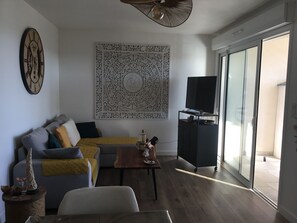 Ein Wohnzimmer mit einer Couch, einem Couchtisch, einer Wanduhr, einem Fernseher auf einem Schrank und einem großen Fenster.
