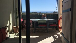 Un balcon avec une table, des chaises, des plantes en pot et une vue sur la mer.
