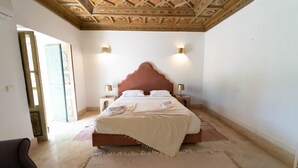 Un dormitorio con una cama grande, dos lámparas de noche, un techo decorativo y vistas a través de un ventanal abierto.