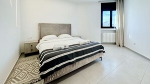 Ein modernes Schlafzimmer mit Bett, Nachttischen, einem Fenster und einer Heizung.